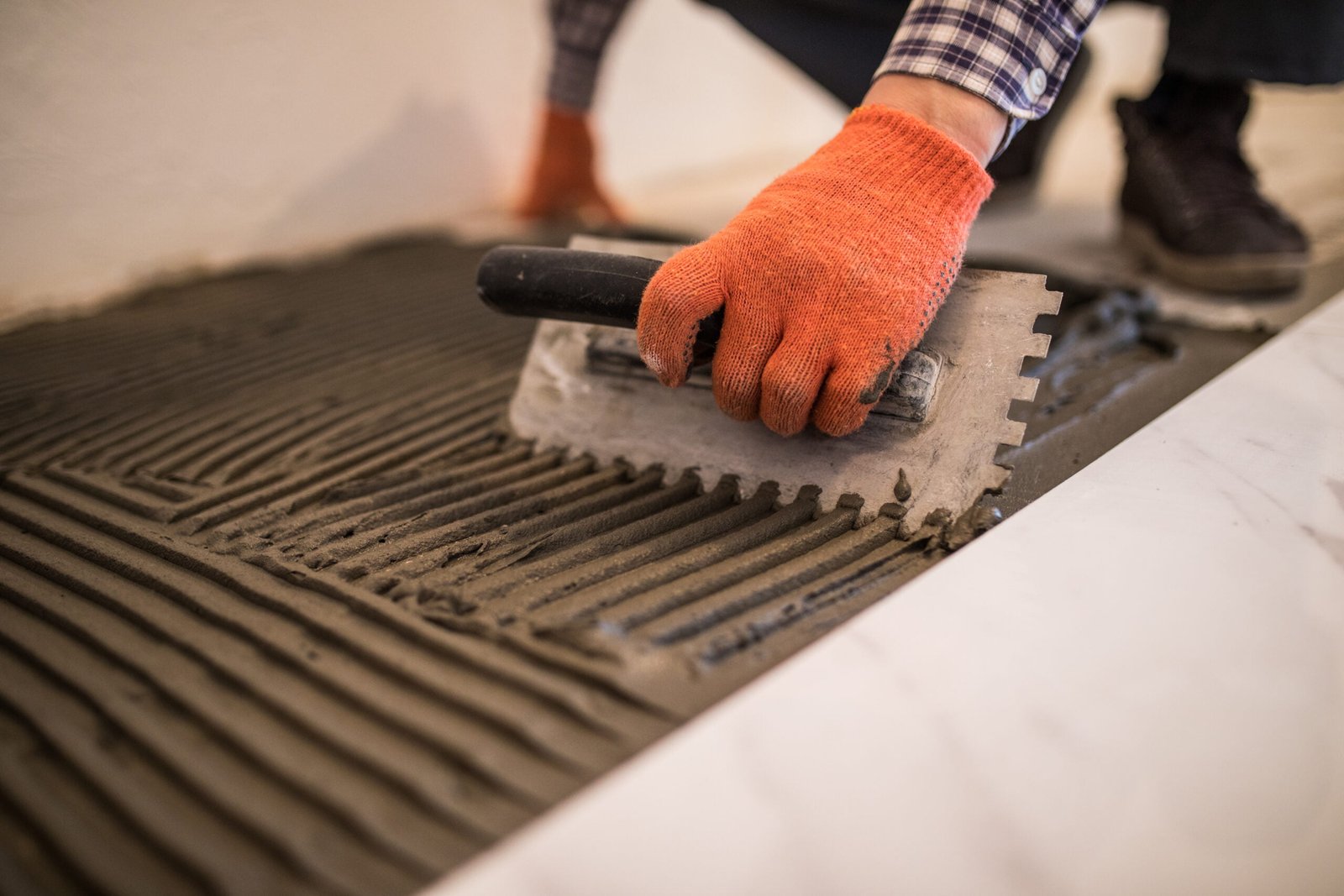 Troweling mortar onto a concrete floor in preparation for laying white floor tile.